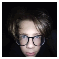 a young boy wearing glasses looks at the camera in a dark room