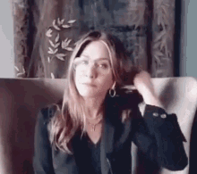 a woman is sitting in a chair with her hand in her hair . she is wearing glasses and a black jacket .