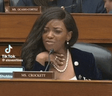 a woman is sitting at a desk in front of a microphone with a name plate that says ms. crockett .