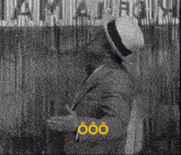 a man in a suit and hat stands in front of a yellow sign that says oão on it