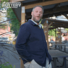 a man in a blue jacket is standing in front of a sign that says the great canadian pottery throw down