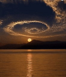 a sunset over a lake with a circular cloud formation in the sky