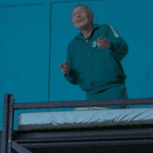 a man in a green jacket is standing on a balcony overlooking a bunk bed .