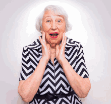 an elderly woman wearing a black and white striped shirt has her mouth open and her hands on her face