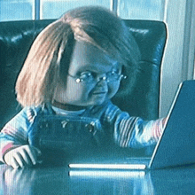 a doll with glasses is sitting at a desk using a laptop