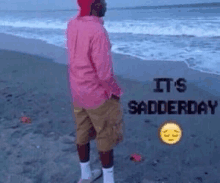 a man in a pink shirt is standing on a beach with the words " it 's sadderday " on the bottom