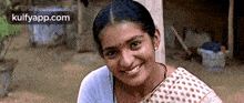 a woman is smiling and looking at the camera while wearing a white shirt and a polka dot saree .