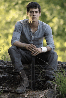 a young man sitting on a log holding a sword