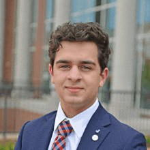 a young man in a suit and tie has a pin on his jacket that says ' j ' on it