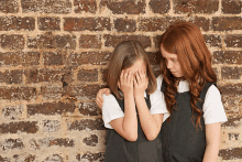 two little girls standing next to each other one covering her face