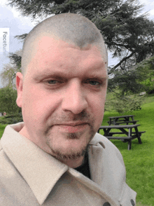 a man with a shaved head and a beard is standing in a park