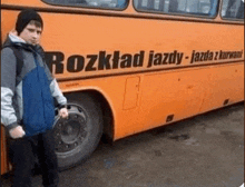 a boy is standing in front of an orange bus that says rozklad jazdy