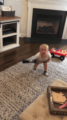 a baby is standing on a rug in front of a fireplace with a red toy that says e on it