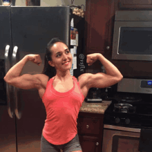 a woman in a red tank top flexes her muscles in front of a refrigerator with a calendar on it