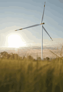 a wind turbine in a grassy field with the sun behind it