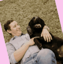 a man is laying on the grass with a black dog