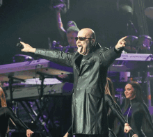 a man in a black leather coat is singing into a microphone with his tongue hanging out