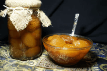 a jar of peaches next to a bowl of peaches with a spoon