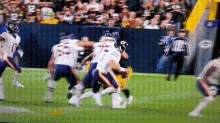 a football game is being played on a field with a referee in the background and a green bay packers logo on the wall