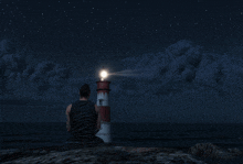 a man sits in front of a lighthouse that is lit up