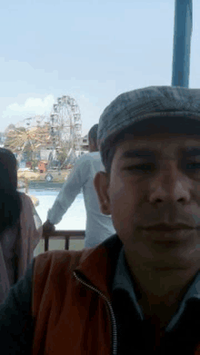 a man in a hat is taking a selfie in front of a ferris wheel .