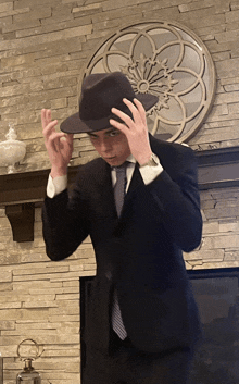 a man in a suit is adjusting his hat in front of a fireplace