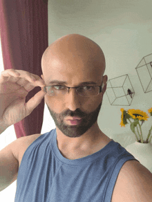 a bald man with a beard wears glasses and a blue tank top