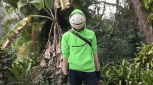 a man wearing a green hoodie and a mask is standing in a jungle