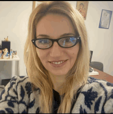 a woman wearing glasses and a blue sweater smiles for the camera