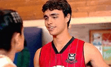 a young man in a red basketball jersey is standing next to a woman in a gym .