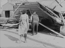 a black and white photo of a man and woman standing in front of a building that says o. ganahi