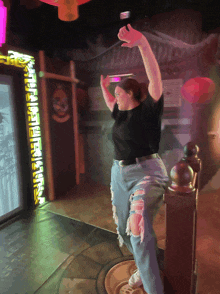 a woman in a black shirt and ripped jeans stands in front of a wall with chinese writing on it