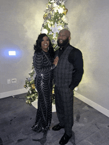 a man and woman are posing in front of a christmas tree