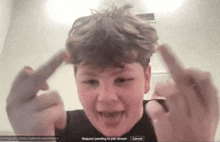 a young boy is giving the middle finger while looking at the camera on a video call .