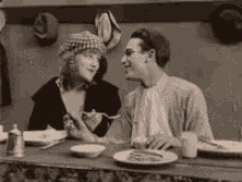 a black and white photo of a man and a woman sitting at a table with plates of food .