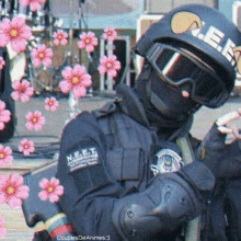 a police officer wearing a helmet , goggles , and gloves is standing in front of pink flowers .