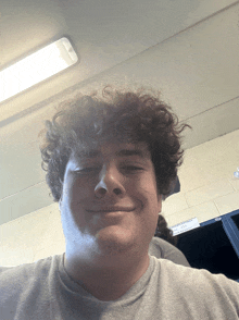 a man with curly hair is smiling in front of a sign that says no smoking in the locker room