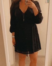 a woman in a black dress takes a selfie in a mirror