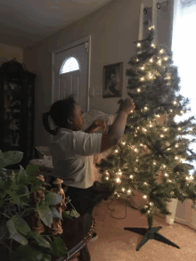 a woman decorates a christmas tree in front of a picture of a man