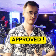 a man in a floral shirt is giving a thumbs up next to a sign that says approved