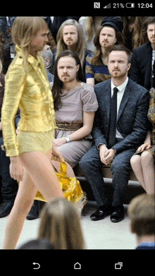 a man in a suit sits in the audience watching a model walk down a runway