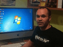 a man wearing a shirt that says estopate sits in front of an apple computer