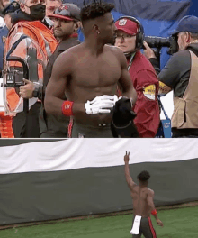 a man without a shirt is standing on a football field while a cameraman takes a picture of him