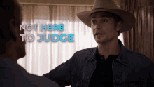 a man in a cowboy hat is talking to another man with the words not here to judge behind him