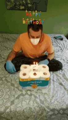 a man wearing a mask and gloves is sitting on a bed next to a birthday cake made out of toilet paper