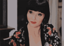 a woman with short black hair and red lipstick is wearing a floral shirt and earrings .