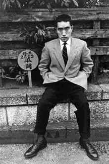 a man in a suit and tie sits in front of a sign that has the number 233 on it