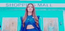 a woman in a blue dress is standing in front of a shopping mall .