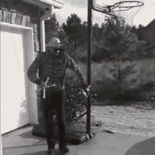 a black and white photo of a man standing next to a basketball hoop in front of a garage door .