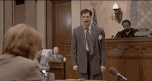 a man in a suit and tie is giving a speech in front of a judge in a courtroom .